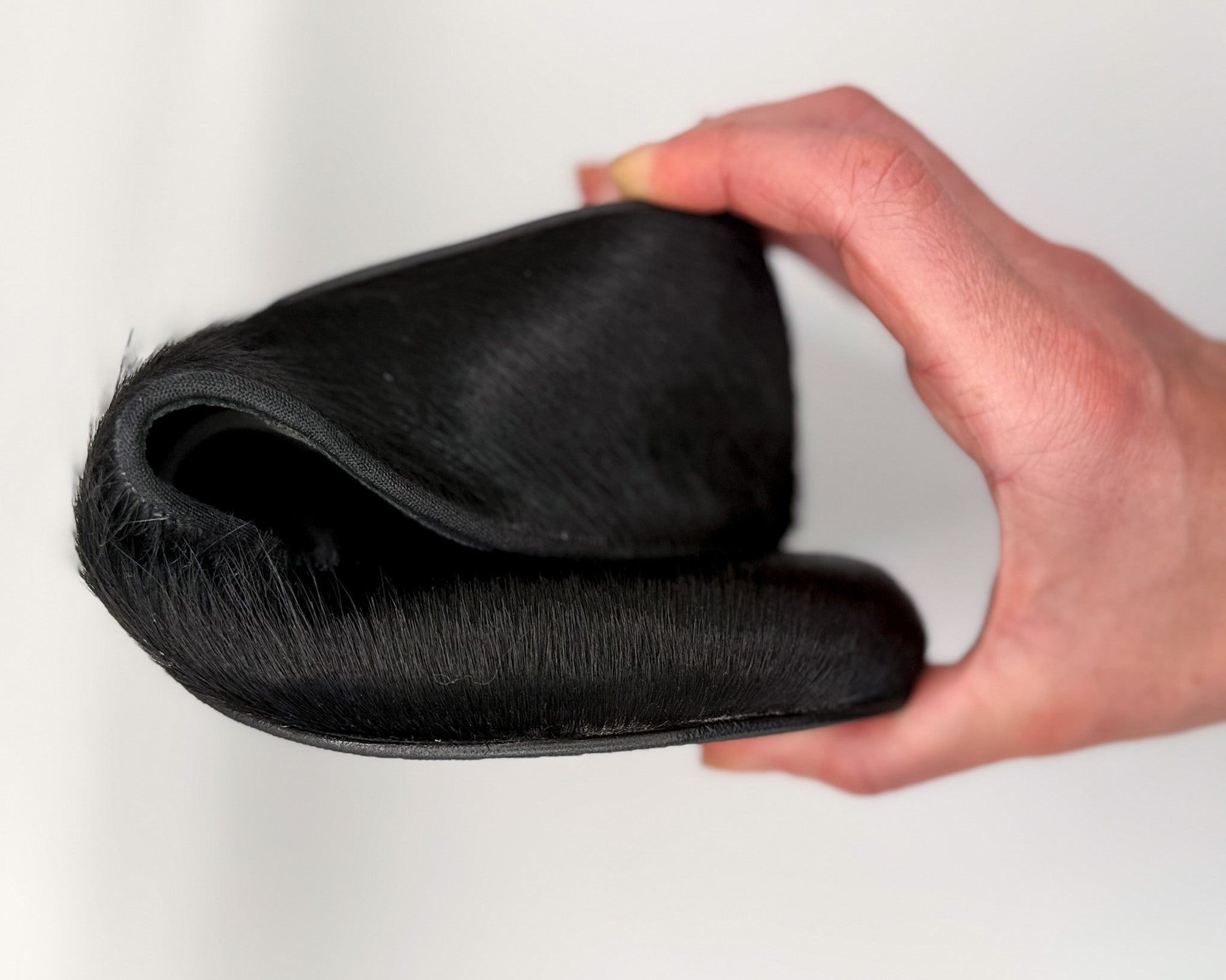 Black hair extension held by a hand against a white background